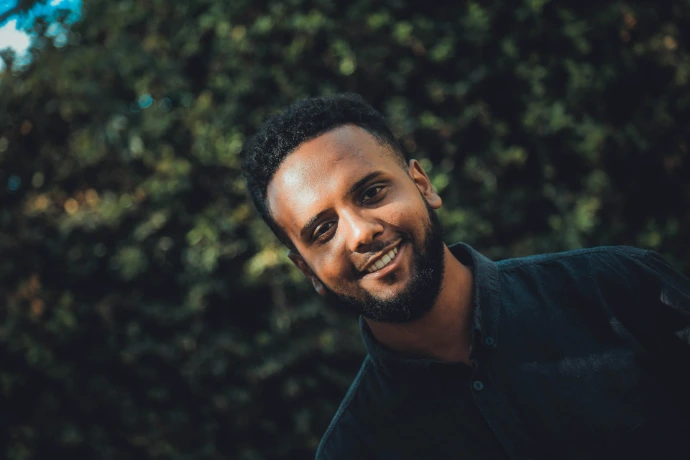 smiling man in blue dress shirt by hedge during daytime
